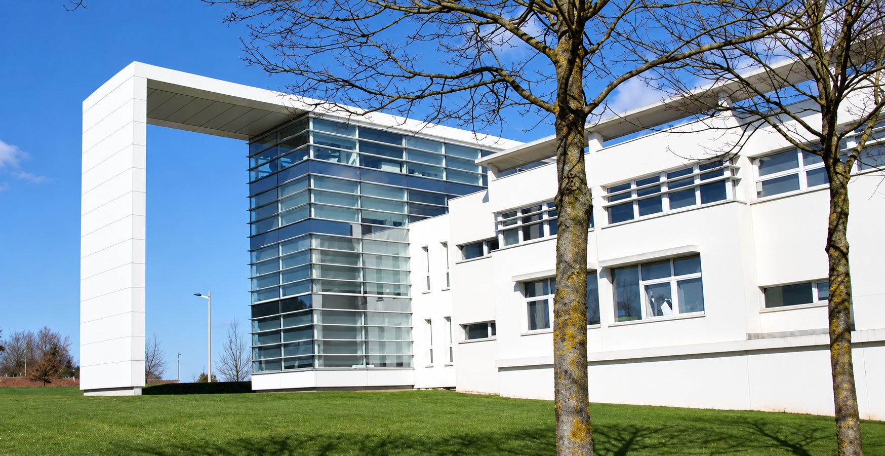 Le bâtiment moderne du cabinet à Amiens : murs blancs, façade vitrée et grand portique sous un ciel bleu.