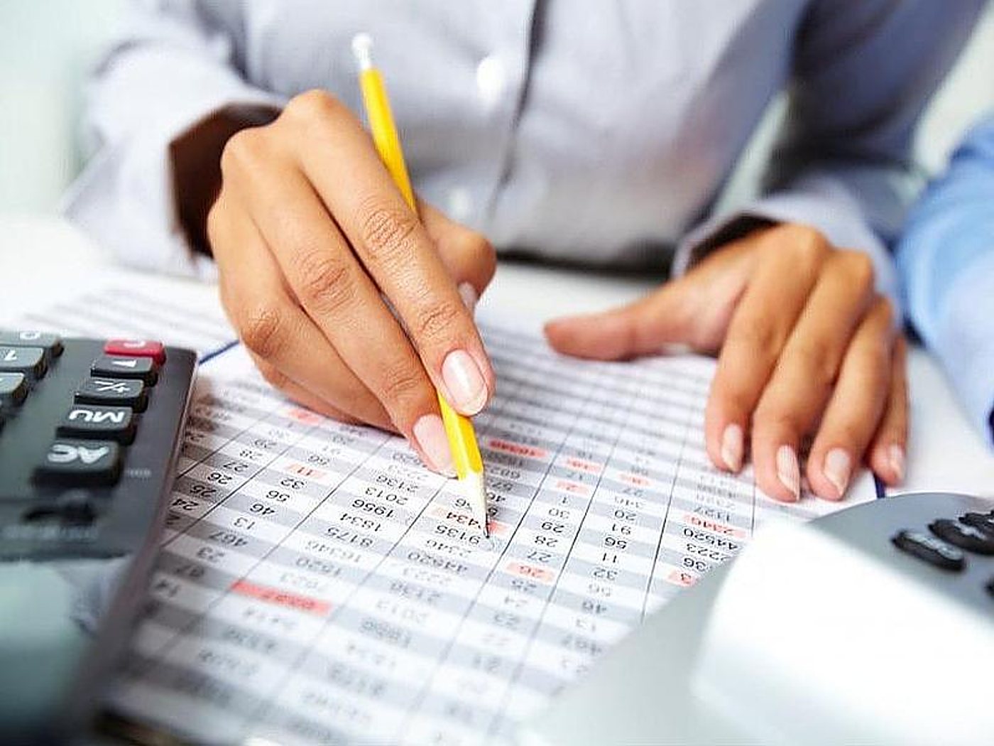 Une personne suit des colonnes de chiffres au crayon sur une feuille de calcul, à côté d’une calculatrice.